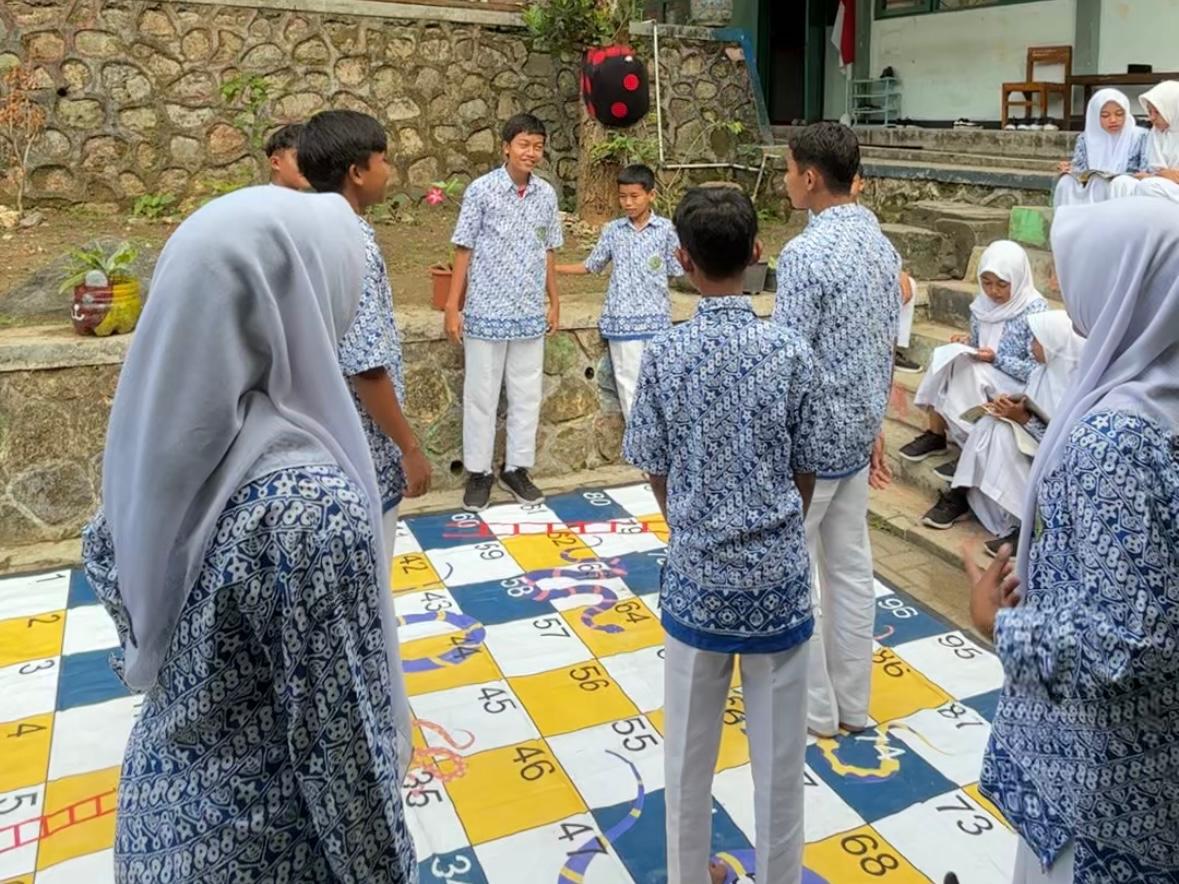 Mata pelajaran IPS di MTsN 3 Kulon Progo, para murid disuguhi pengalaman belajar yang benar-benar menyenangkan (joyful learning) lewat metode asesmen sumatif yang unik: permainan ular tangga, Kamis, (09/10/2025). Dengan rasa semangat dan antusiasme tinggi, siswa dibagi dalam kelompok kecil, masing-masing menugaskan satu anggota sebagai “bidak” dalam permainan menjadi ujung tombak perjuangan kelompok menuju puncak papan permainan. Setiap langkah yang diambil membawa mereka pada soal-soal kreatif yang menguji pemahaman mereka tentang materi inti: Kondisi Geografis dan Pelestarian Sumber Daya Alam, dari letak Indonesia hingga pentingnya menjaga hutan dan laut.